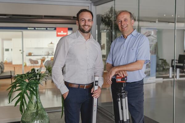 Zwei Bauingenieure stehen mit Vermessungsgeräten in einem modernen Bürogebäude.