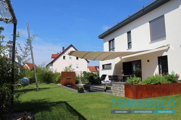 Modernes Einfamilienhaus mit Sonnensegel, gepflegtem Garten und Terrasse im Sommer.