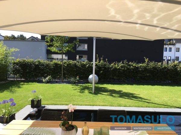 Große Markise spendet Schatten auf moderner Terrasse mit Garten und stilvoller Bepflanzung.