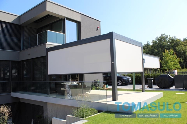 Moderne Terrassenüberdachung mit Markise an einem Einfamilienhaus mit Glasgeländer.