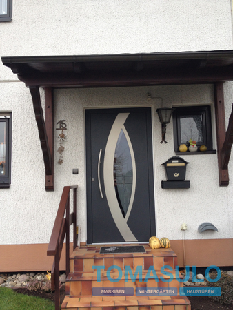 Moderne Haustür mit Glaseinsatz, Vordach, Briefkasten und herbstlicher Dekoration.