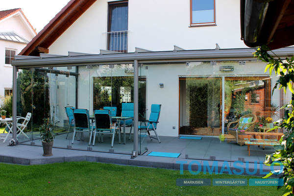 Moderner Wintergarten mit Glaswänden und Gartenmöbeln an Einfamilienhaus im Grünen.