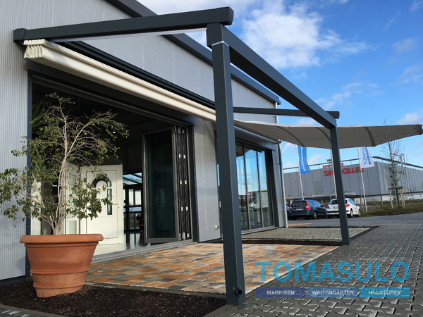 Moderne Terrassenüberdachung mit Markise vor einem Gebäudeeingang und Pflastersteinen.