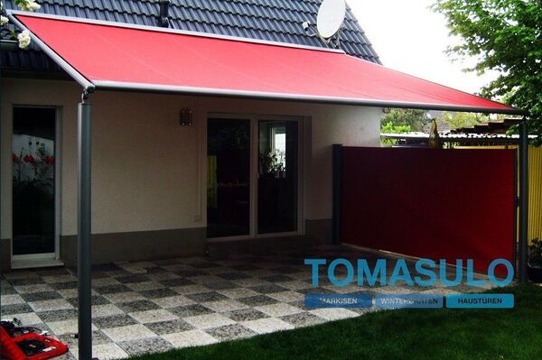 Moderne Terrassenüberdachung mit roter Markise und Sichtschutz an einem Einfamilienhaus.