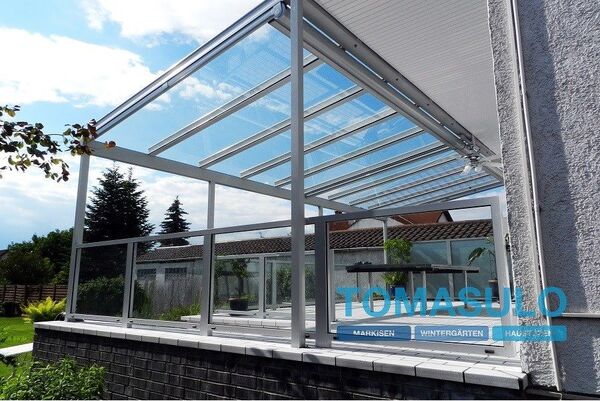 Moderner Wintergarten aus Glas und Aluminium am Haus mit Blick in den Garten.