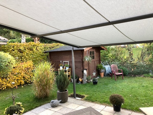 Überdachte Terrasse mit Blick auf gepflegten Garten, Gartenhaus und dekorativen Pflanzen.